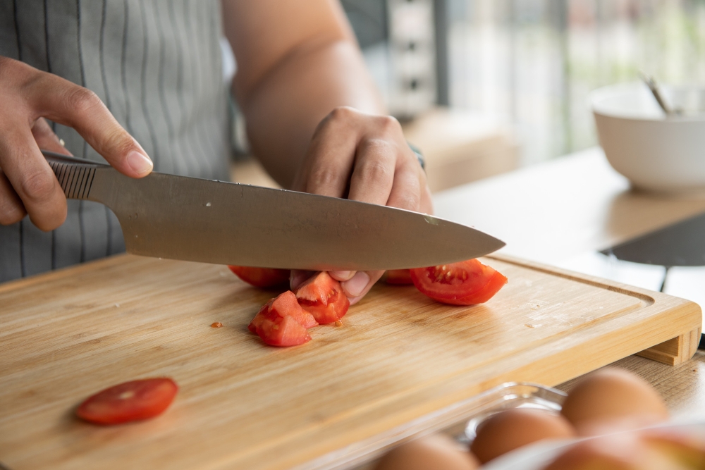 A chef cutting tomatoes on a cutting board in a kitchen.